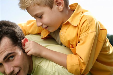 Father giving son a piggyback ride, while son pulls at father's ear Stock Photo - Premium Royalty-Free, Code: 628-00919967