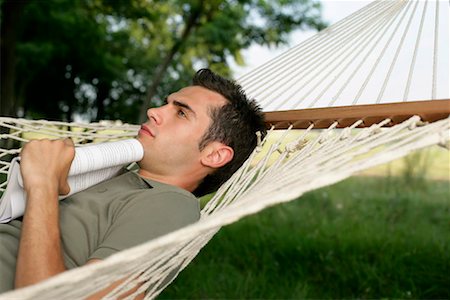 Reflective looking man lying with a book in his hand in a hammock Stock Photo - Premium Royalty-Free, Code: 628-00920031