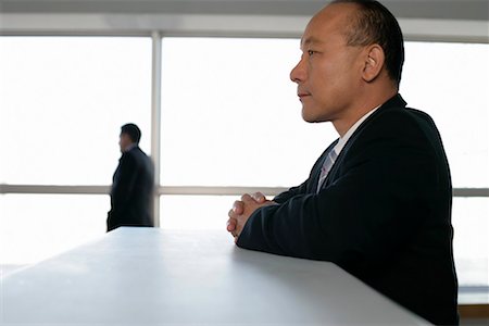 Asian Businessman resting upon a counter with a businessman in the background Stock Photo - Premium Royalty-Free, Code: 628-00920507