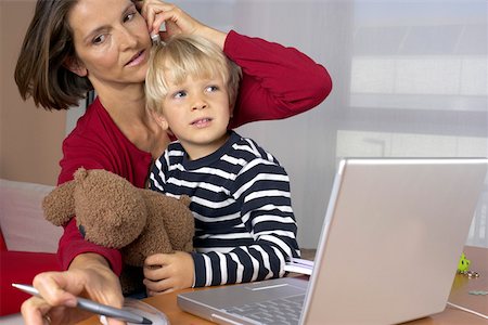 Mother phoning with a mobile phone and taking notes while son (4-5 Years) sitting on her lap Stock Photo - Premium Royalty-Free, Code: 628-01278443