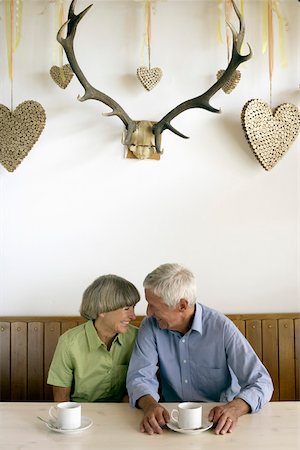Senior adult couple sitting under a decoration of cork hearts while having breakfast Stock Photo - Premium Royalty-Free, Code: 628-01278593