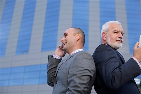 simsearch:628-01279499,k - Two businessmen standing back to back, one phoning with a mobile phone Fotografie stock - Premium Royalty-Free, Codice: 628-01278782