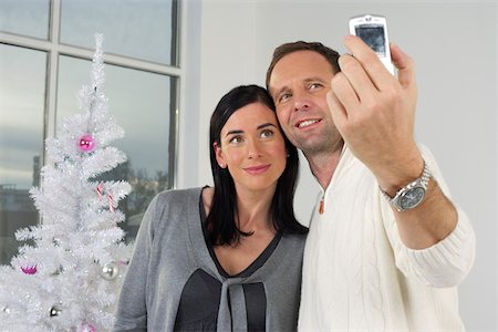 Couple photographing themselves with a mobile phone in front of a white Christmas tree Stock Photo - Premium Royalty-Free, Code: 628-01278854