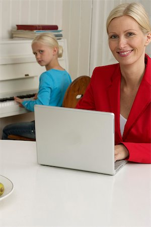 Blond girl is playing piano behind her mother who is working with a laptop, selective focus Stock Photo - Premium Royalty-Free, Code: 628-01278926