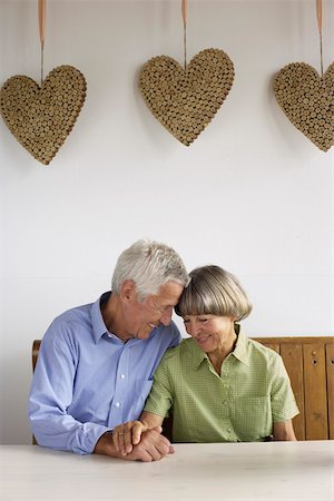 Senior adult couple sitting under a decoration of cork hearts while smiling at one another Stock Photo - Premium Royalty-Free, Code: 628-01279023