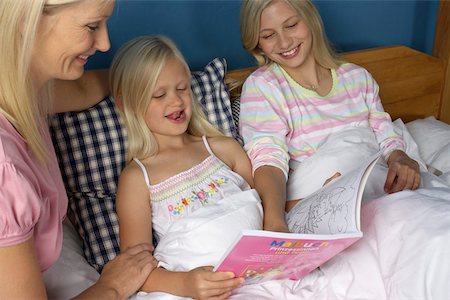 Mother sitting at the bed of her two blond daughters, all looking at a book for children, close-up Foto de stock - Sin royalties Premium, Código: 628-01279030