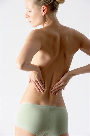 Young blonde woman only wearing a slip with her hands on her back, rear view Stock Photo - Premium Royalty-Free, Code: 628-01279033