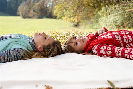 Two young women lying head to head on a sheet in a park, selective focus Stock Photo - Premium Royalty-Free, Code: 628-01279217