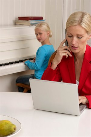 Blond girl is playing piano behind her mother who is working with a laptop, selective focus Stock Photo - Premium Royalty-Free, Code: 628-01279400