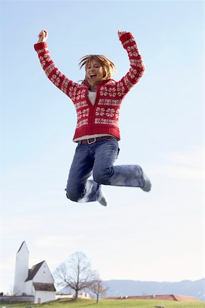 Young woman jumping into the air in front of a small town Stock Photo - Premium Royalty-Free, Code: 628-01279525