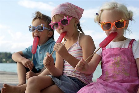 Three children with sunglasses each eating an ice lolly , close- up Foto de stock - Sin royalties Premium, Código: 628-01279541