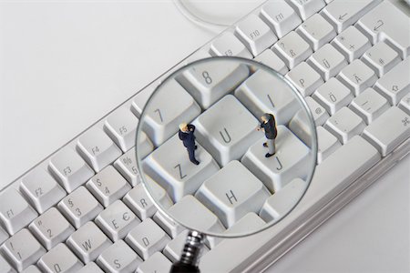 Two businessmen figurines on a computer keyboard, view through a magnifying glass Stock Photo - Premium Royalty-Free, Code: 628-01279732