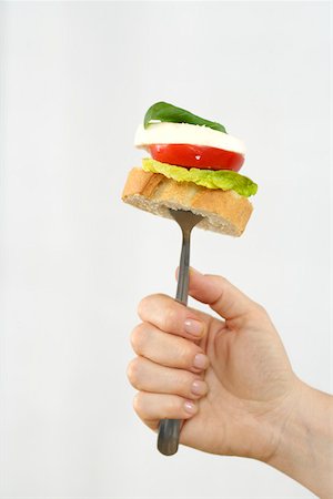 Woman holding a fork with a slice of banquette, lettuce, tomato, mozzarella and basil Stock Photo - Premium Royalty-Free, Code: 628-01494832