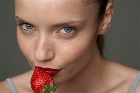 Young woman with a red strawberry under her red lips (part of), close-up Stock Photo - Premium Royalty-Free, Code: 628-01495238