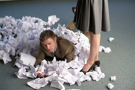 simsearch:628-01639098,k - Businessman lying on heap of crushed papers on floor, businesswoman standing at side Stock Photo - Premium Royalty-Free, Code: 628-01639104