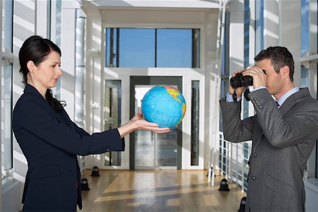 Businessman looking through field glasses to businesswoman holding a globe Stock Photo - Premium Royalty-Free, Code: 628-01639116