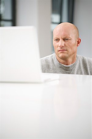 Mature man crouching at a desk looking at laptop Stock Photo - Premium Royalty-Free, Code: 628-01712018