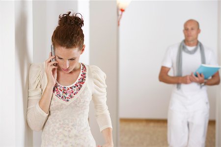 Young woman phoning with a mobile phone, mature man in background Stock Photo - Premium Royalty-Free, Code: 628-01712011