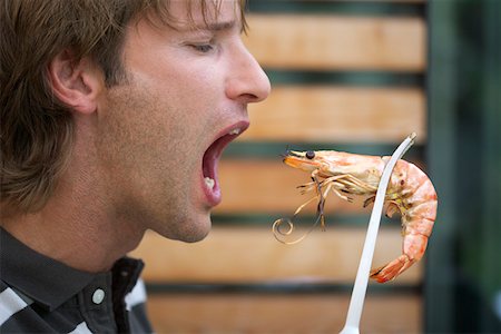 simsearch:628-01712063,k - Man holding a shrimp with gripper near his open mouth Stock Photo - Premium Royalty-Free, Code: 628-01712062