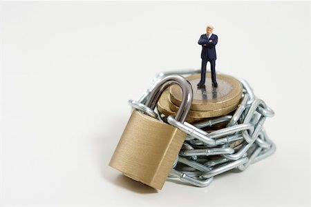 Businessman figurine on a stack of coins wrapped of a chain with a padlock Stock Photo - Premium Royalty-Free, Code: 628-01712337