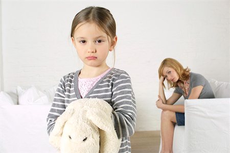 sad child sitting - Cheerless girl looking at camera, mother sitting in background Stock Photo - Premium Royalty-Free, Code: 628-02197920