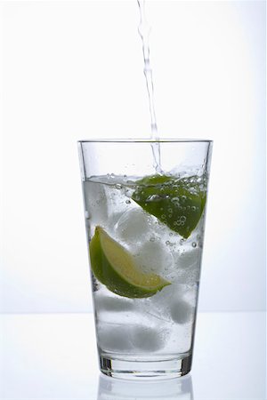 Glass with a slice of lime and ice cubes in it getting filled with water Stock Photo - Premium Royalty-Free, Code: 628-02228107