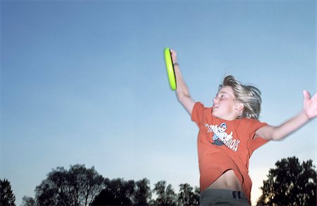 Blonde Boy catching a Frisbee while jumping into the Air - Game - Leisure Time - Youth - Park - Twilight Stock Photo - Premium Royalty-Free, Code: 628-02615725