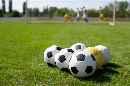 soccer ball closeup - Several soccer balls, soccer players exercising in background Stock Photo - Premium Royalty-Free, Code: 628-02954217