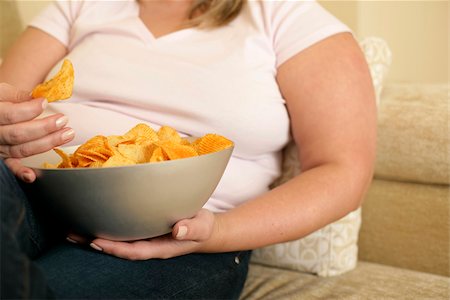 Overweight woman on a settee is eating crips from a bowl (part of), close-up Stock Photo - Premium Royalty-Free, Code: 628-02954490