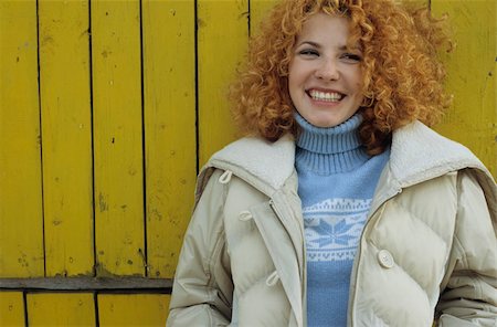 simsearch:628-02954798,k - Young Woman with red curly Hair leaning against a yellow wooden Wall - Winterly Clothing - Season - Facial Expression Fotografie stock - Premium Royalty-Free, Codice: 628-02954635