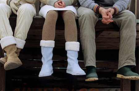 Three Friends sitting next to each other with their Hands folded in their Laps - Wooden Footbridge - Warm Clothing - Season Stock Photo - Premium Royalty-Free, Code: 628-02954659