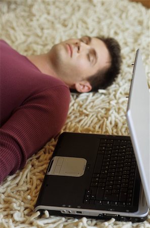 simsearch:628-02954783,k - Jeune homme allongé sur un tapis à côté d'un ordinateur portable - fatigue - Relaxation - technologie - Accueil - salon chambre à coucher Photographie de stock - Premium Libres de Droits, Code: 628-02954775