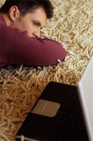 simsearch:628-02954783,k - Jeune homme allongé sur un tapis à côté d'un ordinateur portable - fatigue - Relaxation - technologie - Accueil - salon Photographie de stock - Premium Libres de Droits, Code: 628-02954778