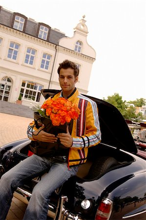 simsearch:628-03201079,k - Young man with black hair sitting on a trunk with a bunch of roses in his hands, selective focus Stock Photo - Premium Royalty-Free, Code: 628-03201058