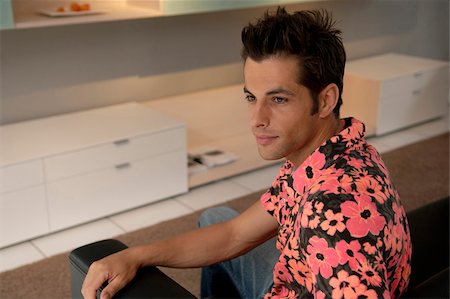 person in hawaiian shirt - Young man with black hair sitting on a settee in front of two modern cupboards, selective focus Stock Photo - Premium Royalty-Free, Code: 628-03201076