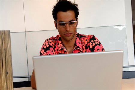 person in hawaiian shirt - Young man with black hair and trendy eyeglasses in a Hawaiian shirt sitting in front of a laptop, selective focus Stock Photo - Premium Royalty-Free, Code: 628-03201080