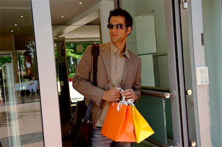simsearch:628-03201079,k - Young man with sunglasses and bags in his hand walking out of a clothes shop Stock Photo - Premium Royalty-Free, Code: 628-03201107