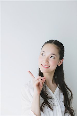 portraits of japanese women - Young woman pointing finger up smiling Stock Photo - Premium Royalty-Free, Code: 622-06964322