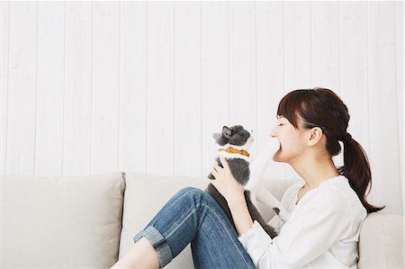 Japanese young woman in jeans and white shirt with cat on the sofa Stock Photo - Premium Royalty-Free, Code: 622-07743582