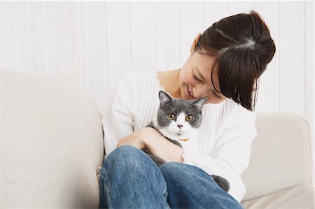 Japanese young woman in jeans and white shirt with cat on the sofa Foto de stock - Sin royalties Premium, Código: 622-07743583