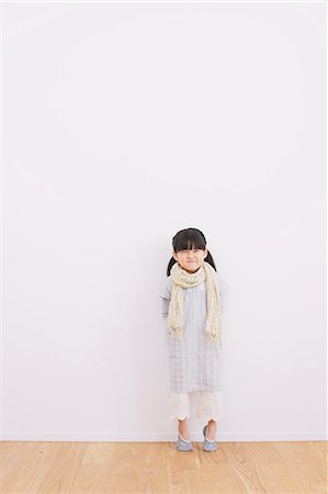 Elementary age girl leaning against a white wall and smiling at camera Stock Photo - Premium Royalty-Free, Code: 622-08139018