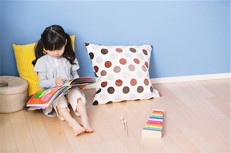 Elementary age girl reading an illustrated book on the floor of the kids room Stock Photo - Premium Royalty-Free, Code: 622-08139134