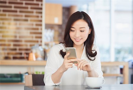 Japanese woman with smartphone in a stylish cafe Stock Photo - Premium Royalty-Free, Code: 622-09014338