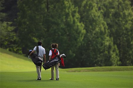 Rear view of a couple walking on the fairway as they carry their golf bags Stock Photo - Premium Royalty-Free, Code: 622-00806971