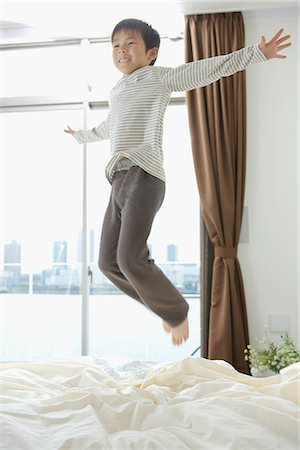 Boy smiling and jumping on his bed Stock Photo - Premium Royalty-Free, Code: 622-02759094