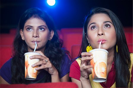 Two female friends enjoying soft drinks while watching movie in a cinema hall Foto de stock - Sin royalties Premium, Código: 630-06724528