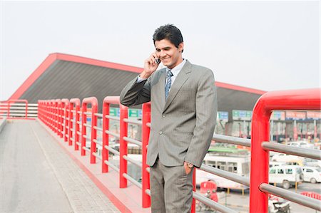 Businessman standing on a footbridge and talking on a mobile phone, Gurgaon, Haryana, India Stock Photo - Premium Royalty-Free, Code: 630-06724613