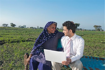 Businessman sitting in the field near his mother and using a laptop, Sonipat, Haryana, India Foto de stock - Sin royalties Premium, Código: 630-06724695