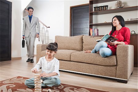 ethnic couples at home on sofa - Girl playing Jenga with her parents in the background Stock Photo - Premium Royalty-Free, Code: 630-06723008