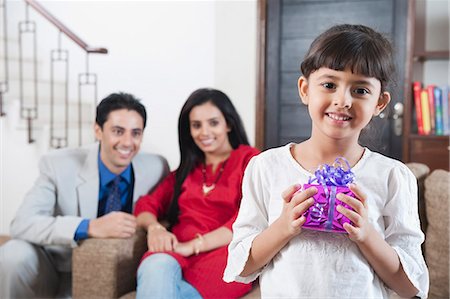 parents couple indian - Portrait of a girl holding a gift with her parents in the background Foto de stock - Sin royalties Premium, Código: 630-06723018